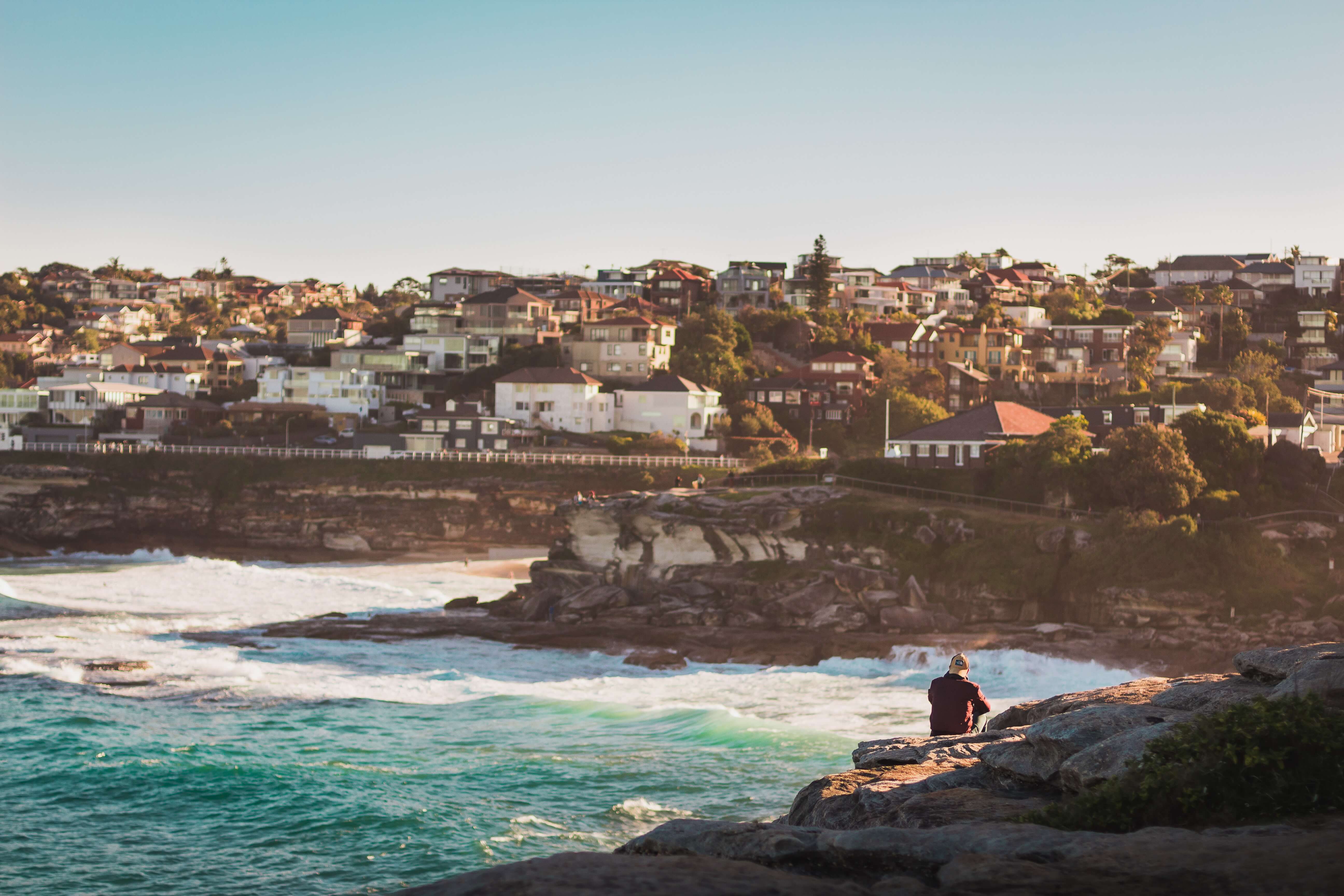 photography of man sitting on rock formation front of city